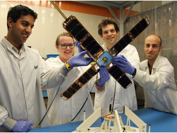 Four Students Wearing Lab Coats Showing the Solar Arrays of a Satellite