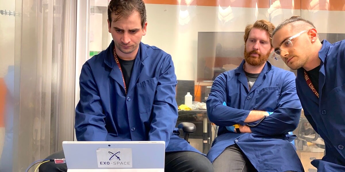 Three researchers wearing lab coats staring at computer