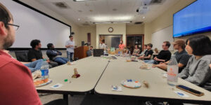 Group of people seating around table eating and conversing inside classroom