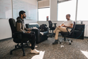 People seated on office chairs in the middle of an office engaged in conversation