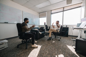 People seated on office chairs in the middle of an office engaged in conversation